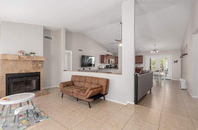 living room featuring lofted ceiling, a fireplace, ceiling fan with notable chandelier, and light tile patterned floors