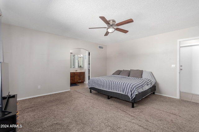 carpeted bedroom featuring ceiling fan, a textured ceiling, and ensuite bath