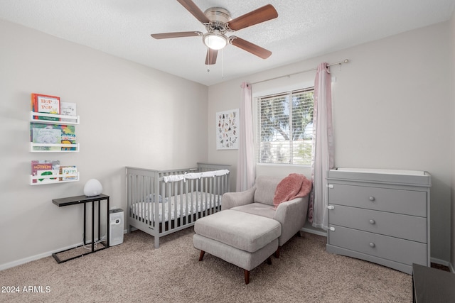 bedroom with ceiling fan, a textured ceiling, light colored carpet, and a nursery area