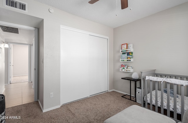 bedroom with a closet, carpet, a nursery area, a textured ceiling, and ceiling fan