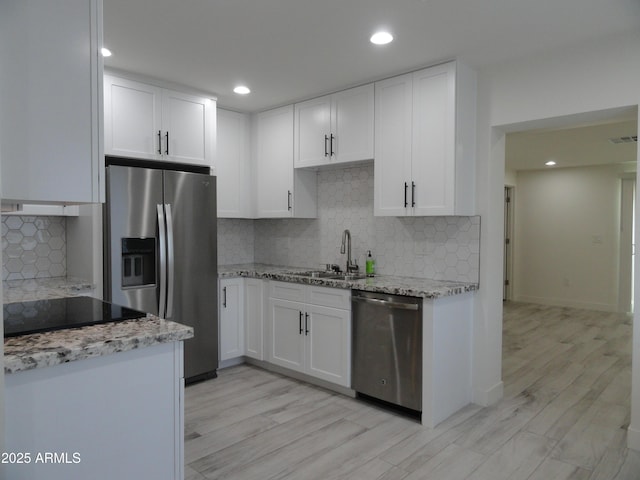 kitchen featuring appliances with stainless steel finishes, a sink, decorative backsplash, light stone counters, and white cabinetry