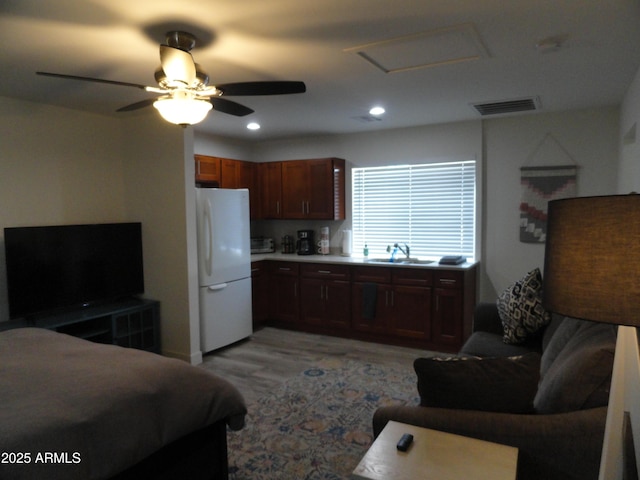 bedroom featuring freestanding refrigerator, attic access, light wood-style flooring, a sink, and a ceiling fan
