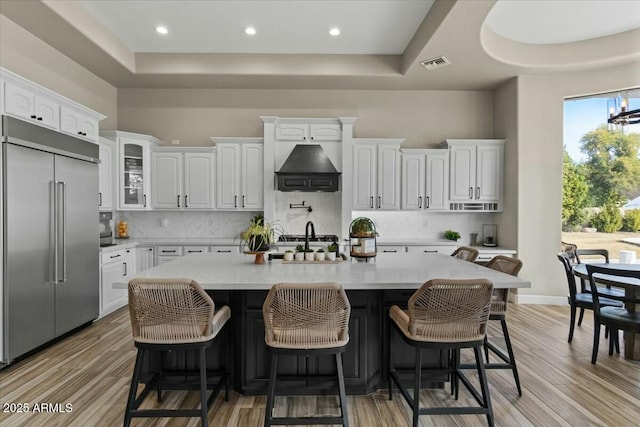 kitchen featuring stainless steel built in fridge, white cabinets, light hardwood / wood-style flooring, and an island with sink