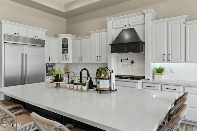 kitchen featuring white cabinets, custom exhaust hood, an island with sink, tasteful backsplash, and a breakfast bar