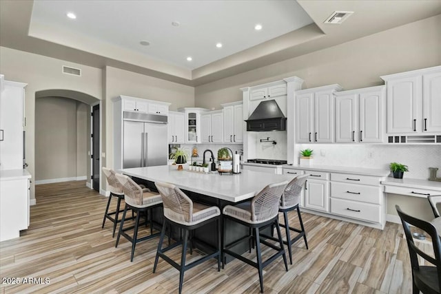 kitchen featuring premium range hood, white cabinets, a breakfast bar, and an island with sink