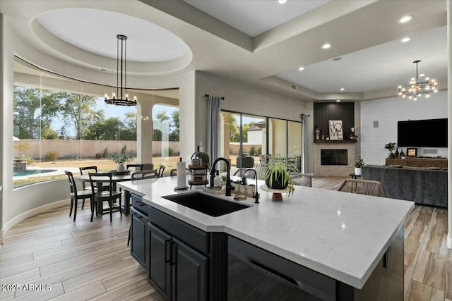 kitchen featuring sink, an island with sink, a raised ceiling, and hanging light fixtures