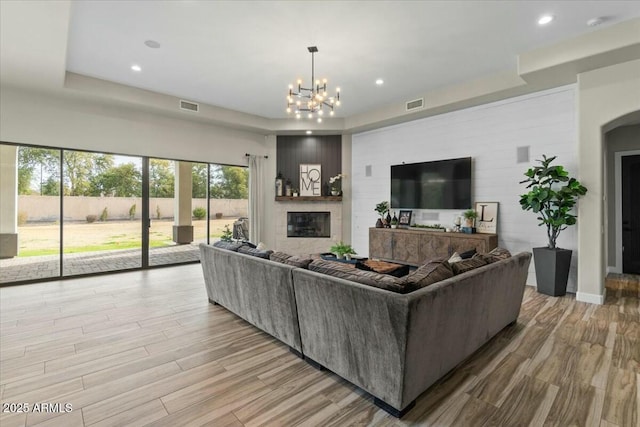 living room with a large fireplace, a tray ceiling, light hardwood / wood-style flooring, and a chandelier