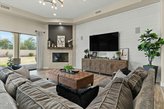 living room with a large fireplace, light hardwood / wood-style flooring, and a chandelier