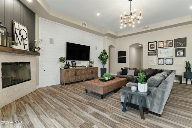 living room with light hardwood / wood-style floors, wooden walls, an inviting chandelier, and a fireplace