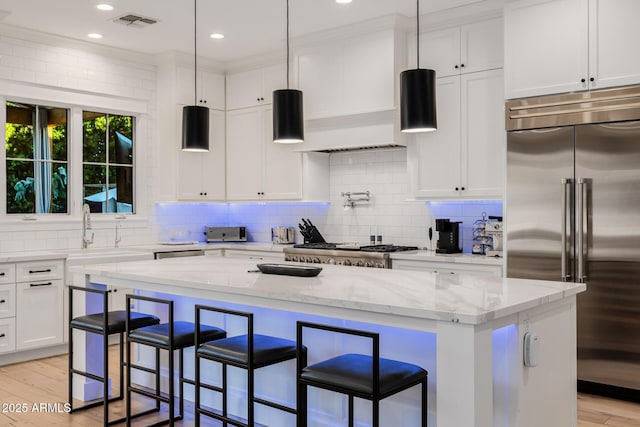 kitchen featuring light stone counters, hanging light fixtures, built in fridge, a kitchen island, and white cabinets