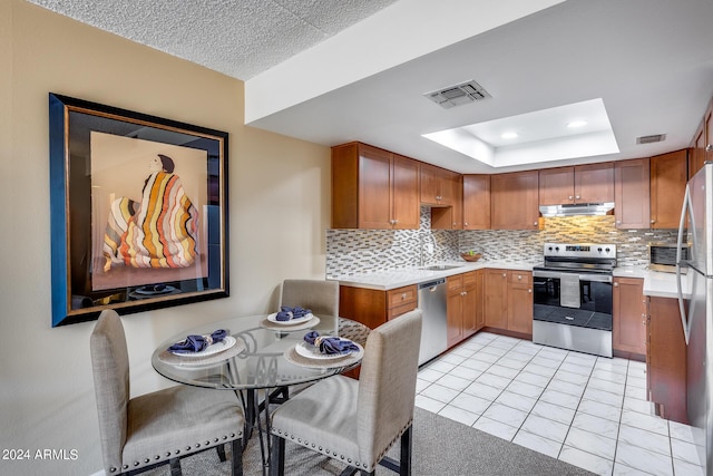 kitchen with sink, a tray ceiling, light tile patterned flooring, decorative backsplash, and stainless steel appliances