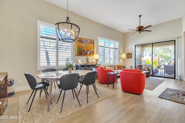 dining space with ceiling fan with notable chandelier, vaulted ceiling, and light hardwood / wood-style floors