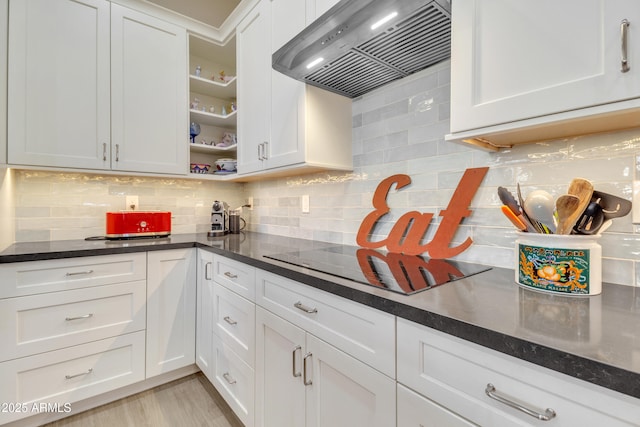 kitchen featuring wall chimney range hood, light hardwood / wood-style floors, white cabinets, black electric cooktop, and decorative backsplash