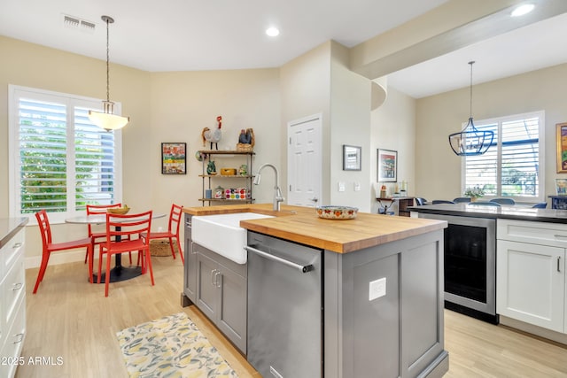 kitchen with pendant lighting, an island with sink, wooden counters, beverage cooler, and stainless steel dishwasher