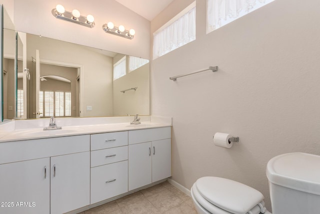 bathroom with toilet, double vanity, baseboards, and a sink