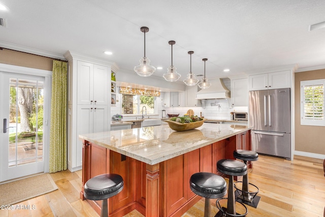 kitchen featuring custom exhaust hood, a kitchen island, high quality fridge, and white cabinetry