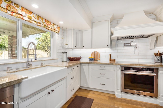 kitchen with white cabinets, oven, and custom exhaust hood