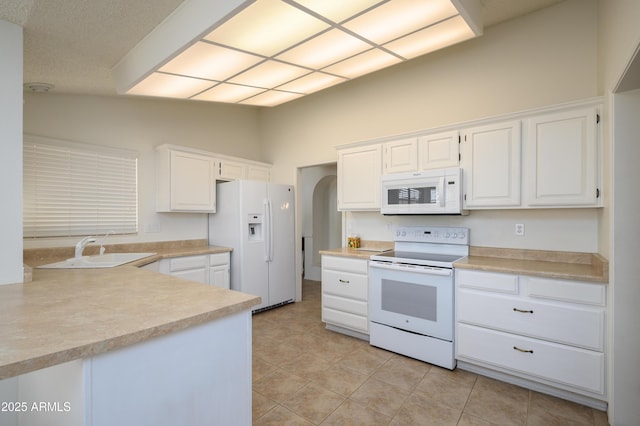 kitchen featuring sink, white cabinetry, vaulted ceiling, kitchen peninsula, and white appliances