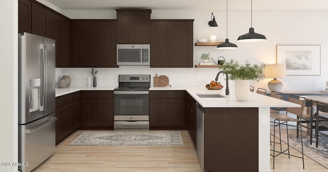 kitchen featuring pendant lighting, a breakfast bar, sink, light wood-type flooring, and stainless steel appliances