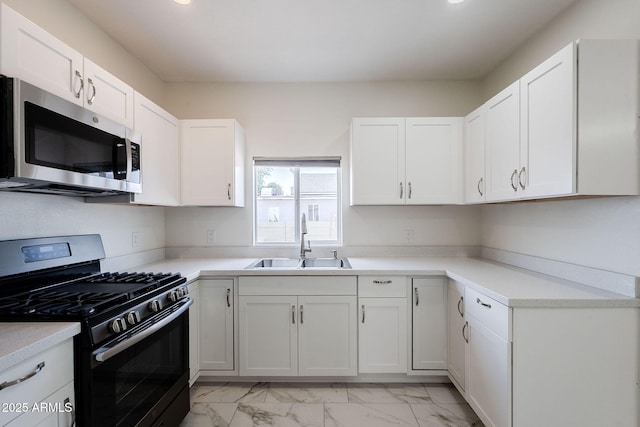 kitchen with a sink, appliances with stainless steel finishes, white cabinetry, and marble finish floor