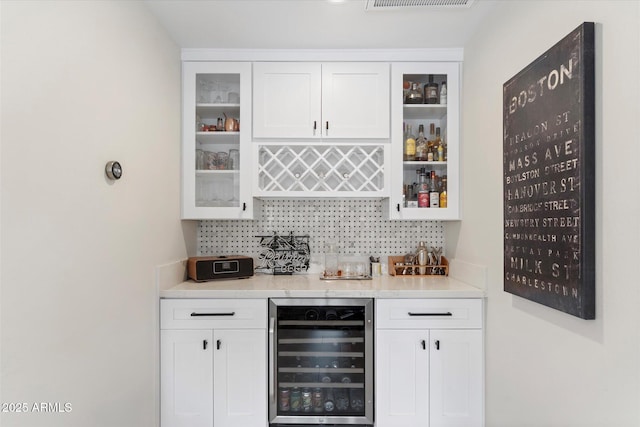 bar featuring decorative backsplash, visible vents, beverage cooler, and a dry bar