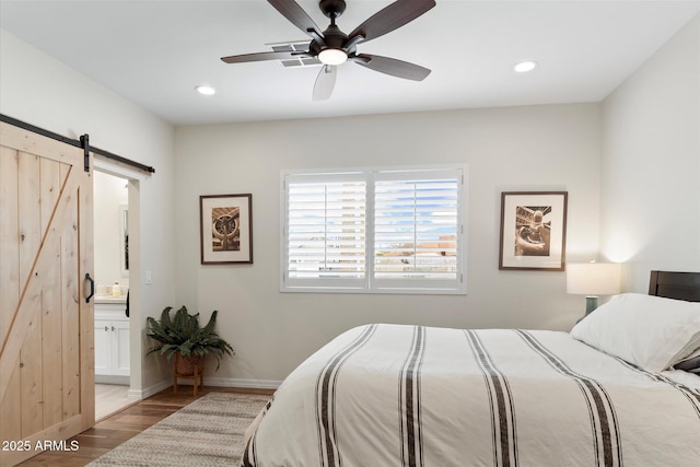 bedroom with a barn door, light wood-style flooring, recessed lighting, and baseboards