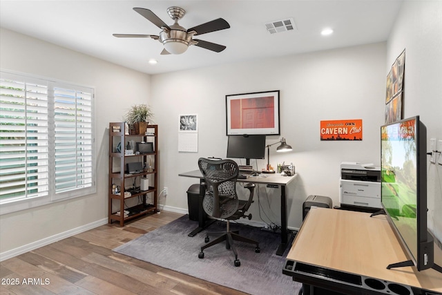 home office with a wealth of natural light, visible vents, wood finished floors, and a ceiling fan