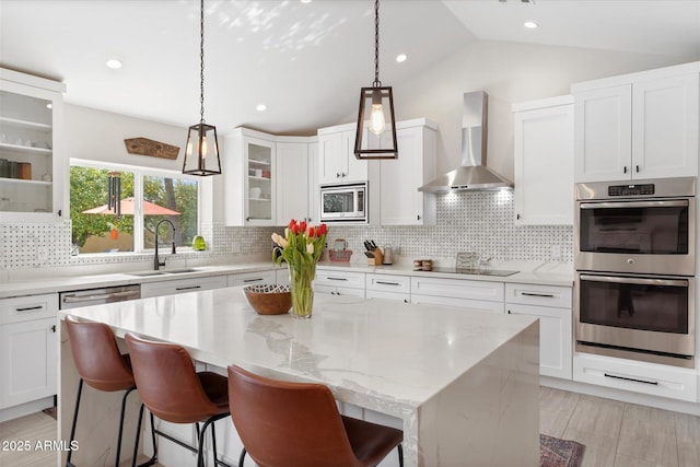 kitchen with a sink, appliances with stainless steel finishes, white cabinets, wall chimney range hood, and glass insert cabinets