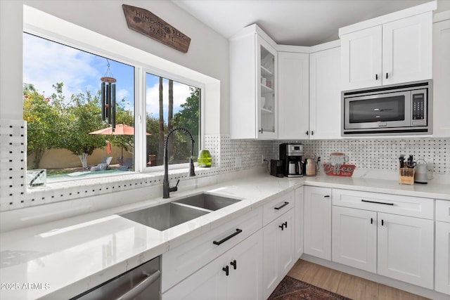 kitchen with backsplash, appliances with stainless steel finishes, glass insert cabinets, and a sink