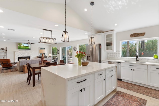 kitchen featuring visible vents, a warm lit fireplace, a sink, ceiling fan, and stainless steel appliances