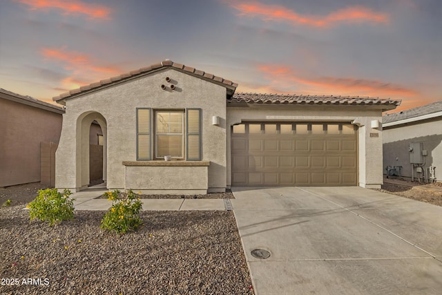 mediterranean / spanish house featuring driveway, an attached garage, a tiled roof, and stucco siding