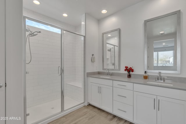 full bath featuring double vanity, a shower stall, a sink, and wood finished floors