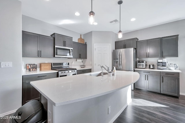 kitchen with an island with sink, stainless steel appliances, dark hardwood / wood-style floors, decorative light fixtures, and sink