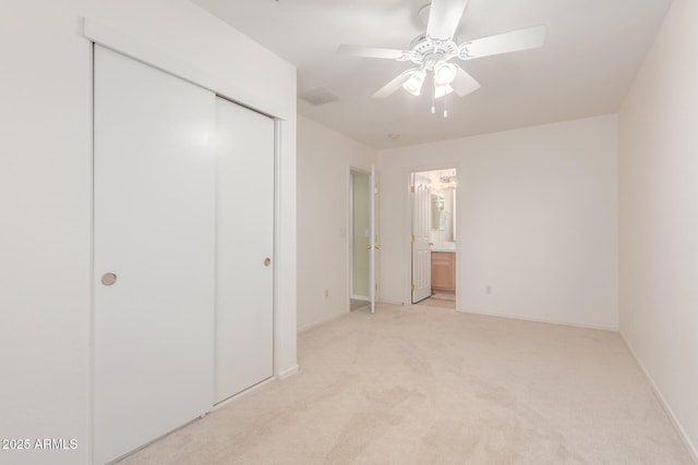 unfurnished bedroom featuring baseboards, ceiling fan, light colored carpet, ensuite bathroom, and a closet