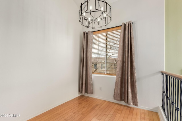 unfurnished room featuring an inviting chandelier, baseboards, and wood-type flooring