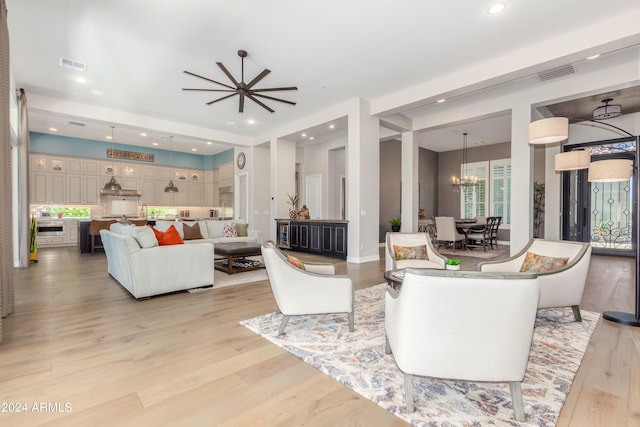 living room with ceiling fan with notable chandelier and light wood-type flooring