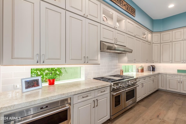 kitchen with tasteful backsplash, white cabinetry, appliances with stainless steel finishes, and light hardwood / wood-style flooring