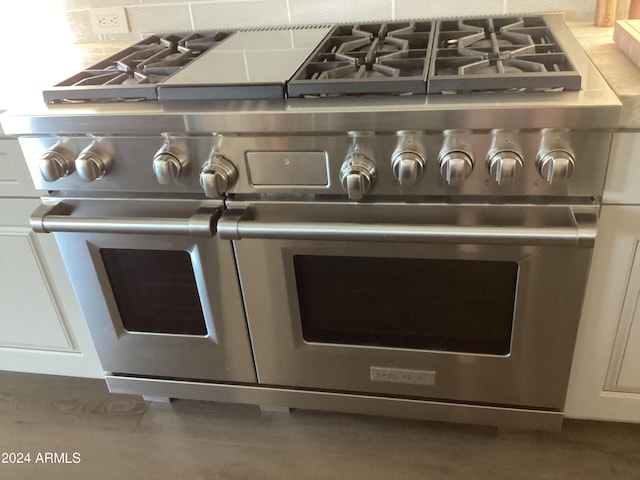 interior details featuring backsplash, white cabinetry, and range with two ovens