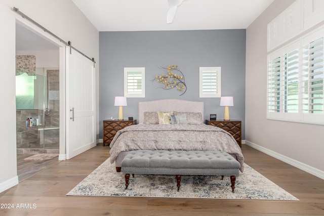 bedroom featuring ceiling fan, a barn door, light hardwood / wood-style flooring, and ensuite bath