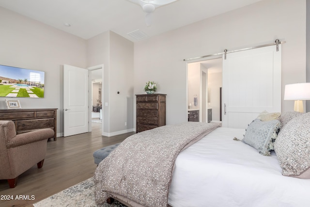 bedroom featuring hardwood / wood-style floors, a barn door, ceiling fan, and connected bathroom