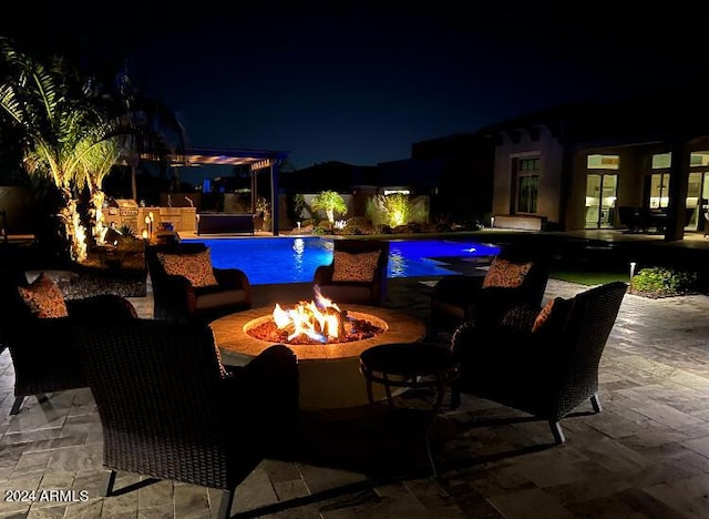 pool at night featuring a fire pit and a patio area