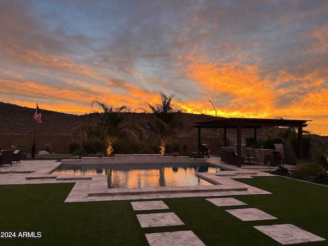 pool at dusk featuring a lawn, outdoor lounge area, and a patio