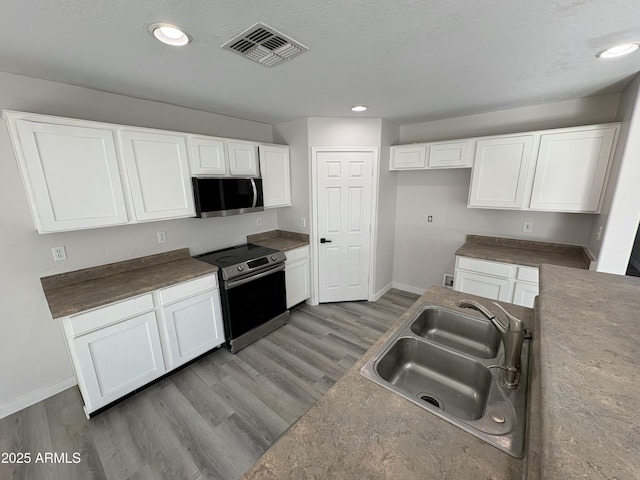 kitchen featuring wood-type flooring, stainless steel appliances, white cabinetry, and sink