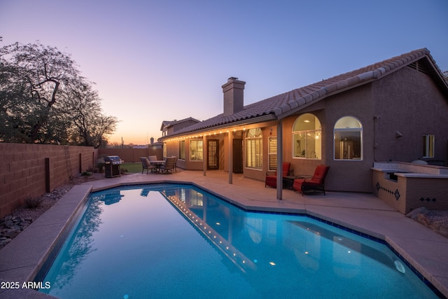 pool at dusk with grilling area and a patio