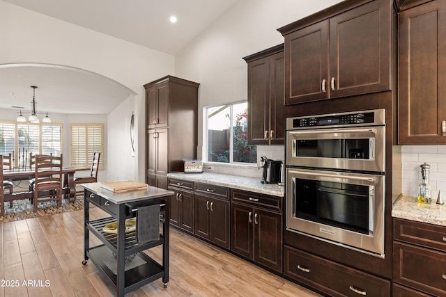 kitchen featuring tasteful backsplash, stainless steel double oven, dark brown cabinetry, and light stone countertops