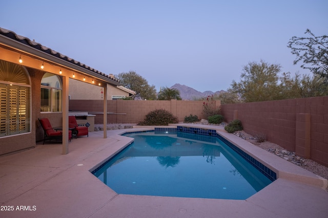 pool at dusk featuring a patio and a mountain view