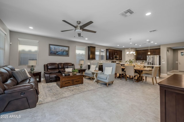 living area featuring ceiling fan with notable chandelier, plenty of natural light, and visible vents