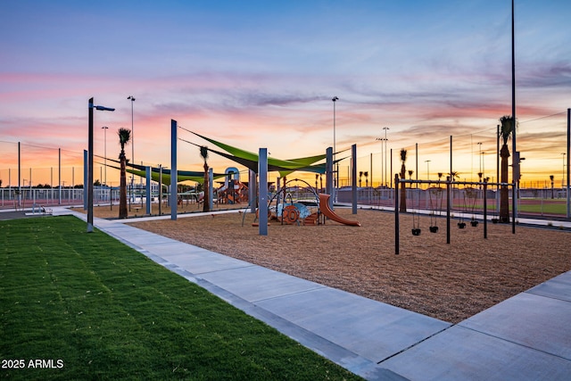 playground at dusk with playground community, a lawn, and fence