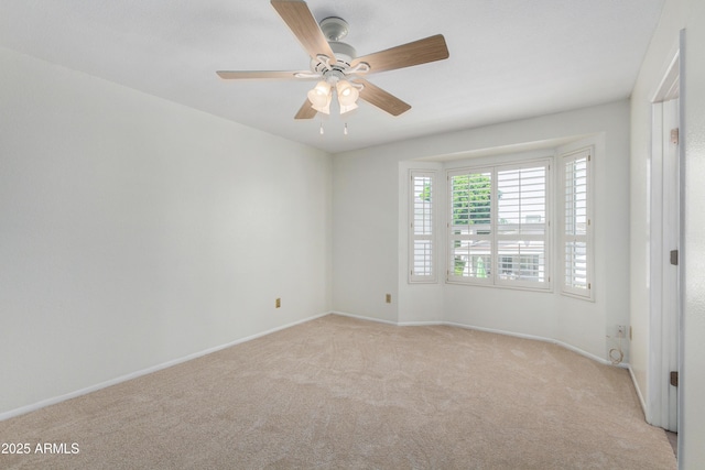 spare room with a ceiling fan, light colored carpet, and baseboards