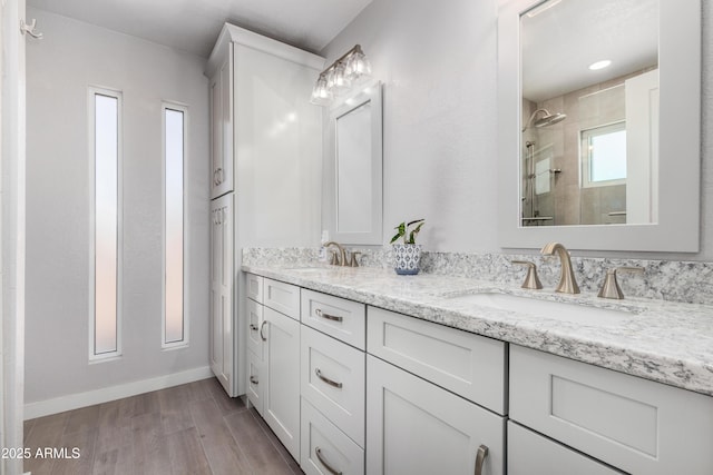 full bathroom featuring double vanity, a sink, tiled shower, and wood finished floors